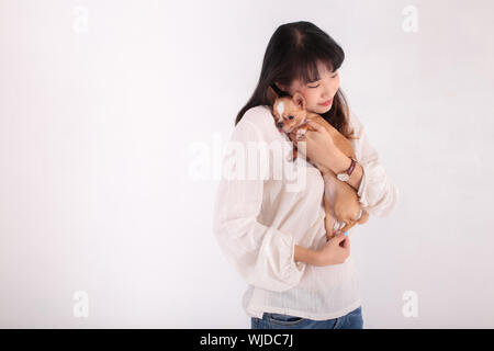 Junge asiatische Frau umarmt adorable Chihuahua Hund und schließen die Augen, während gegen den weißen Hintergrund stehen Stockfoto