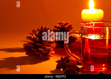 roter Tee in ein Glas, Zimtstangen, Sternanis und einem Nadelbaum Kegel bei Kerzenschein Stockfoto