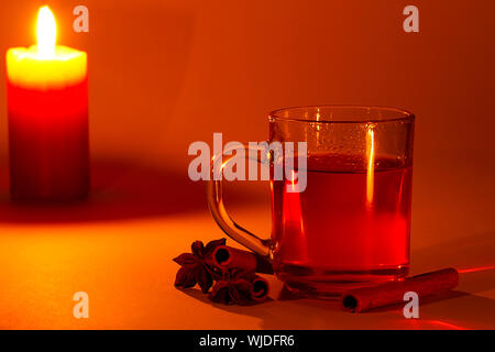 roter Tee in ein Glas, Zimtstangen und Sternanis bei Kerzenschein Stockfoto