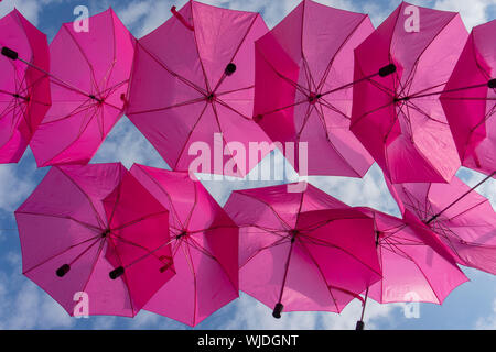 Zwei Reihen von bunten hellen rosa Sonnenschirme gegen einen bewölkten Himmel bis auf die Griffe von unten Stockfoto