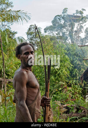 ONNI DORF, Neuguinea, Indonesien - Juni 24: Das Porträt Leon - Korowai Mann mit Bogen und Streiks auf der natürlichen, grünen Wald Hintergrund. Am 24. Juni Stockfoto