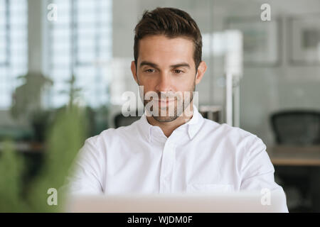 Lächelnde junge Unternehmer, die an einem Notebook arbeitet in seinem Büro Stockfoto