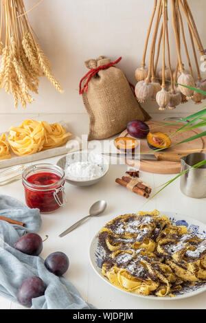 Süße Nudeln Dessert, Nudeln mit Mohn, Pflaumenkompott aus frischen Pflaumen, dunklen Hintergrund, weiße Holztisch mit frischen Blumen dekoriert. Trockene wh Stockfoto