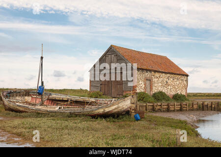 Ein Bild von einem alten Kohle Scheune und Fischerboot auf einer Wasserstraße bei Thornham, Norfolk, England, UK. Stockfoto