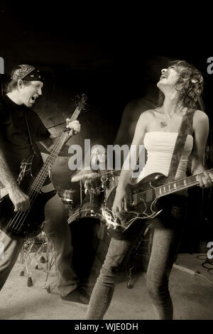 Band spielt auf einer Bühne. Männliche bassist mit weiblichen Gitarrist und Schlagzeuger. Shot mit Strobes und Slow Shutter Speed Beleuchtung Atmosphäre und Bl zu erstellen Stockfoto