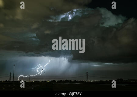 Eine leistungsstarke lightningbolt Streiks in der Erde aus eine dramatische Gewitterwolke Stockfoto