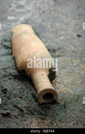 Die alte Flasche liegt am Ufer des kleinen Flusses in Durchsickern. Stockfoto
