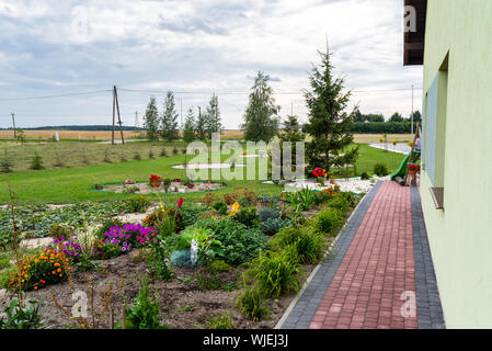 Home Garten mit verschiedenen Arten von bunten Blumen an der Fassade des Gebäudes platziert. Sichtbar Kind auf der Folie und Bäumen. Stockfoto