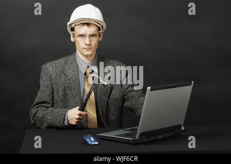 Der Mann, der einen Helm mit einem Hammer im Begriff war, den Computer zu reparieren. Stockfoto