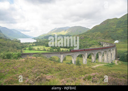 Glenfinnan Viadukt mit dem Dampfzug auf es, mit dem Blick auf den Himmel See und die umliegenden Berge rund um Stockfoto