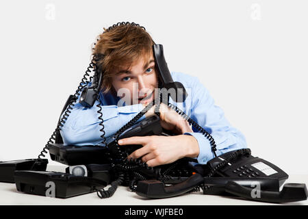Junger Mann sitzt mit einem Bündel von Handys über ihn Stockfoto