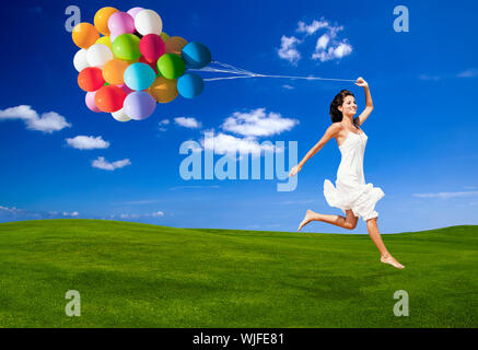 Schöne Frau laufen und springen auf einer grünen Wiese mit bunten ballons Stockfoto