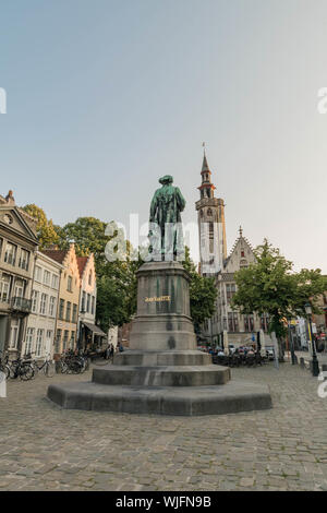 Die Jan Van Eyck Monument Schuß von der Rückseite, mit einem hohen Kirchturm im Hintergrund in Brügge, Belgien. Stockfoto