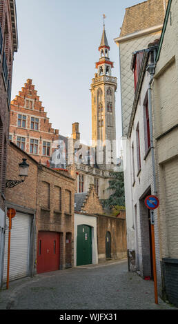 Schmale, gebogene gepflasterten Straße mit alten Häusern aus Stein und einem hohen, schmalen Kirchturm mit einem spitzen oben, Brügge, Belgien Stockfoto