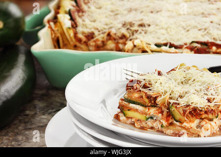 Eine Umhüllung von Zucchini Lasagne mit frischen Zucchini und Kasserolle im Hintergrund. Stockfoto
