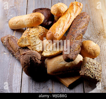 Die Anordnung der verschiedenen verschiedene Brötchen, Baguette, Mohn und Sesam Brötchen, Roggen und Vollkornbrot isoliert auf Hartholz Hintergrund Stockfoto