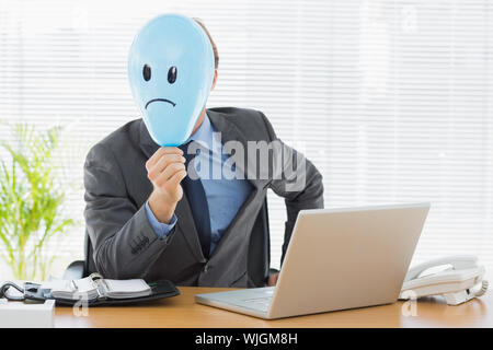 Portrait einer jungen Geschäftsmann Holding traurige Smiley Ballon im Büro Schreibtisch konfrontiert Stockfoto