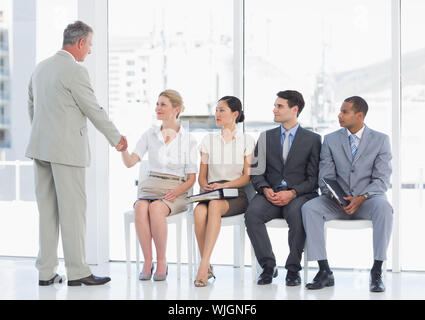 Geschäftsmann Händeschütteln mit Frau neben Menschen warten auf Job Interview in einem hellen Büro Stockfoto