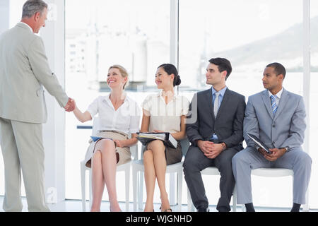 Geschäftsmann Händeschütteln mit Frau neben Menschen warten auf Job Interview in einem hellen Büro Stockfoto