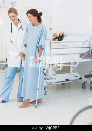Volle Länge von einem Arzt helfen Patienten in Krücken im Krankenhaus Stockfoto
