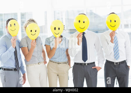 Gruppe von Geschäftsleuten mit glücklichem Lächeln vor den Gesichtern in einem hellen Büro Stockfoto