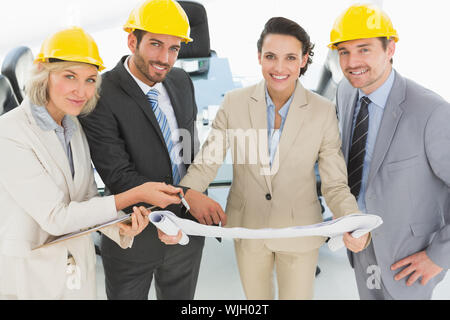 Portrait von gut gekleideten zuversichtlich Architekten mit Schutzhelmen und Blaupause steht im Büro Stockfoto
