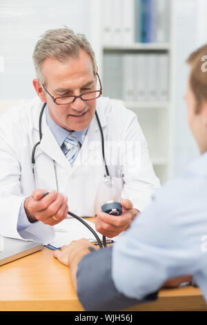 Lächelnd Arzt seine Patienten Blutdruck in seinem Büro im Krankenhaus Stockfoto