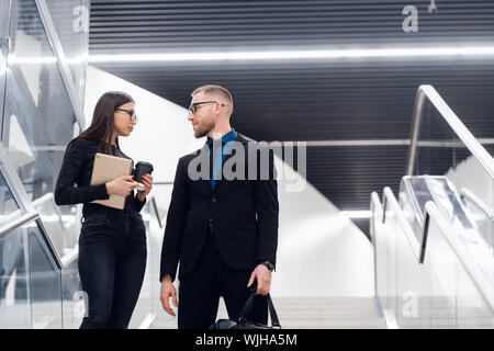 Junge Geschäftsleute stehen auf einer Treppe und Sprechen im modernen Bürogebäude. Frau mit Tablet-PC Stockfoto