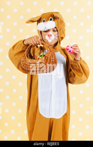 Kind verkleidet als Ostern Hase mit Korb Eiern auf gelben gestrichelten Hintergrund Stockfoto