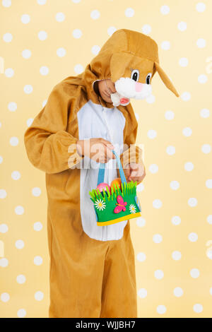 Kind verkleidet als Ostern Hase mit Korb Eiern auf gelben gestrichelten Hintergrund Stockfoto