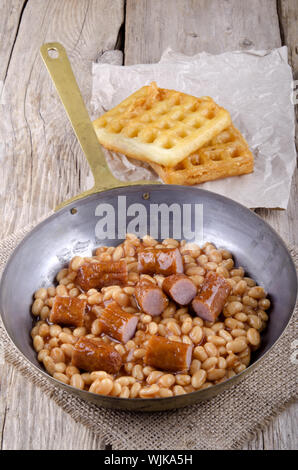 gebackene Bohnen mit Bratwurst und nach Hause gemachte Waffeln in einer Pfanne Stockfoto