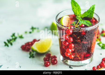 Kalte rote Cocktail mit Johannisbeeren, Limette, Minze, Thymian und Eis im Glas auf hellgrau Betonoberfläche Tabelle. Sommer und alkoholfreien Cocktails. Alcoho Stockfoto