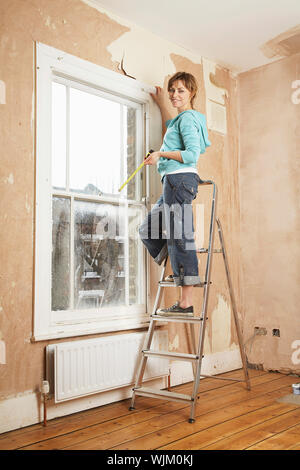 Portrait von Frau mit Maßband beim Stehen auf der Leiter in Unsanierten Haus Stockfoto