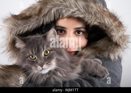 Closeup Porträt der jungen Frau im Pelzmantel mit Kapuze Holding cat auf grauem Hintergrund Stockfoto