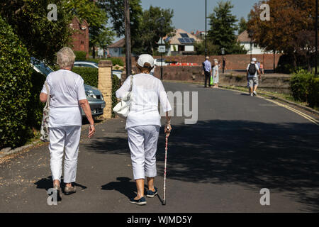 Zwei ältere Frauen gehen auf die Straße, eine der Frauen ist mit einem Spazierstock oder Gehhilfe Stockfoto