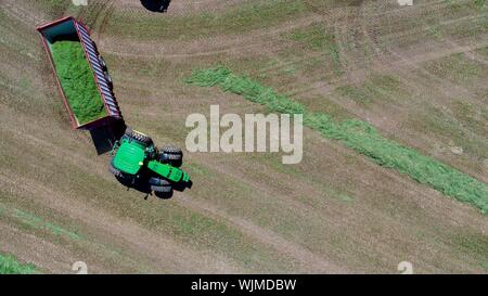Luftaufnahme, direkt über, von John Deere Tractor Pulling Ladewagen, auf der Farm Luzerne Feld außerhalb Monroe, Wisconsin, USA Stockfoto