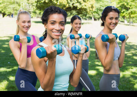 Group Portrait von zuversichtlich sportliche Frauen heben die Hände Gewichte im Park Stockfoto