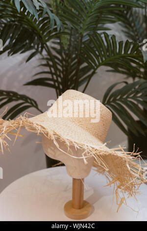 Stroh Hut auf einem Mannequin. Braunen Hut auf leeren Mannequin in einem Speicher auf einem Hintergrund aus Palmblättern. Stockfoto