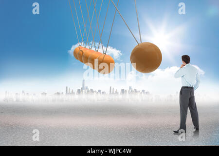 Nachdenklich Geschäftsmann mit der Hand am Kinn gegen Newtons Wiege vor Ort in der Wüste Stockfoto
