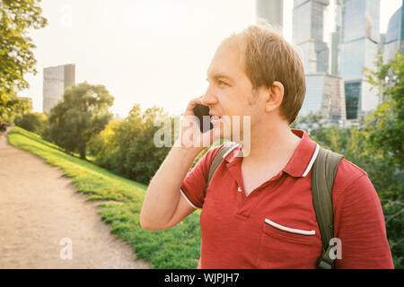 Ein Mann in einem roten T-Shirt mit Rucksack ist, am Telefon zu sprechen Stockfoto