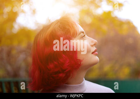 Schöne Frau mit rot gefärbten Haaren und den Hintergrund von Herbst gelbe Blätter. Stockfoto