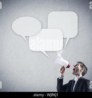 Wütend junger Geschäftsmann schreien in Megaphon vor grauem Hintergrund Stockfoto