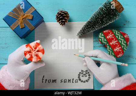 Ansicht von oben Santa Claus Vorbereitung ein Schreiben mit der linken Hand ein Eis mit einigen Weihnachtsverzierungen Stockfoto