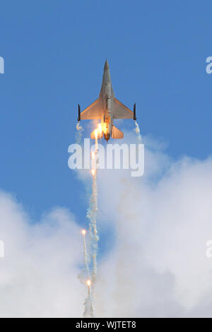 Ein General Dynamics F-16 Fighting Falcon der belgischen Luftwaffe klettert senkrecht und Tropfen flares, wie es die Wolken für den klaren, blauen Himmel verlässt. Stockfoto