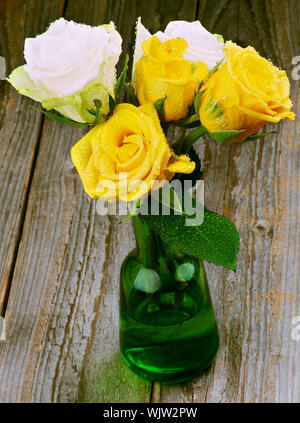 Blumenstrauß aus gelben und weißen Rosen mit Tröpfchen in grünem Glas Vase closeup auf rustikalen Holzmöbeln Hintergrund Stockfoto