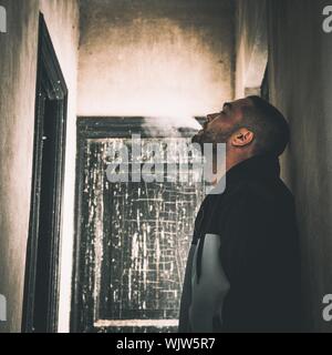 Seitenansicht der nachdenkliche Mensch weisser Rauch lehnte sich an der Wand im alten Haus