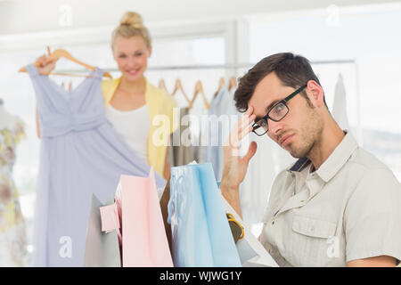 Langweilig Mann sitzt mit Tüten, während Frau Auswahl Kleid im Hintergrund Stockfoto