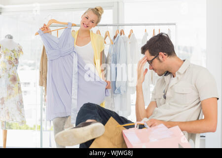 Langweilig Mann sitzt mit Tüten, während Frau Auswahl Kleid im Hintergrund Stockfoto
