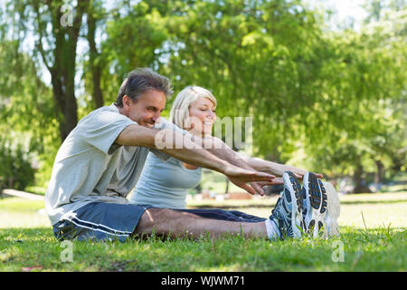 Glückliches Paar stretching während der Sitzung auf dem Rasen im Park Stockfoto