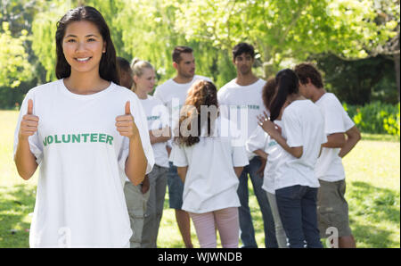 Portrait von zuversichtlich freiwillige Gestik Daumen hoch im Park mit Freunden im Hintergrund Stockfoto